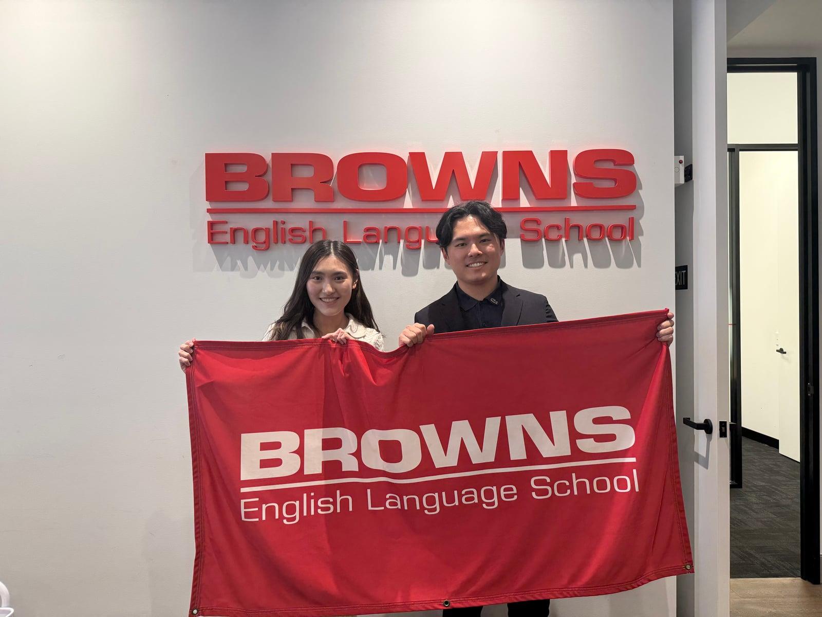 Browns ブリスベン校で、学校の旗を持った学校担当者と成功する留学の代表が撮影した写真