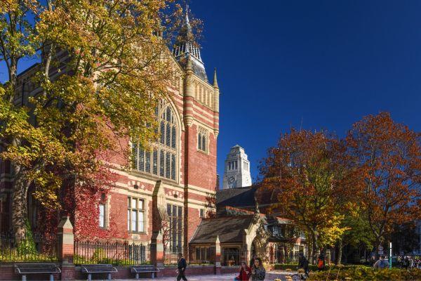 The Unversity of Leeds Great Hall, a grand redbrick building, with the white clock tower of the Parkinson Building visible behind it.
